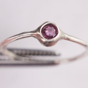 Pu&ograve; includere: Un anello d'argento con una piccola pietra preziosa rotonda di colore viola incastonata in una fascia testurizzata.