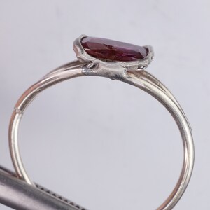 Pu&ograve; includere: Un anello d'argento con una pietra preziosa di colore viola scuro incastonata in una montatura a castone. L'anello &egrave; composto da due bande che sono intrecciate tra loro.