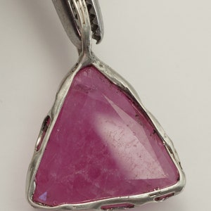 May include: A silver pendant featuring a triangular pink gemstone set in a bezel setting.