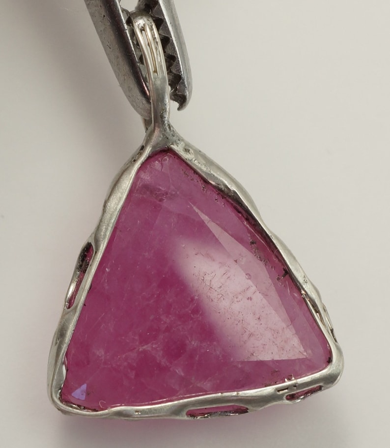 May include: A silver pendant featuring a triangular pink gemstone set in a bezel setting.