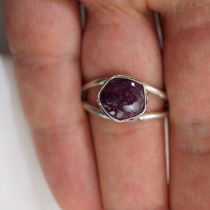 May include: A silver ring with a purple gemstone set in a bezel setting. The ring has a double band design.