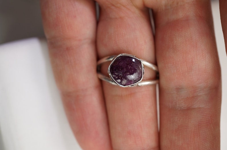 May include: A silver ring with a purple gemstone set in a bezel setting. The ring has a double band design.