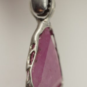 May include: A pink gemstone pendant with a silver setting. The gemstone is faceted and has a triangular shape.