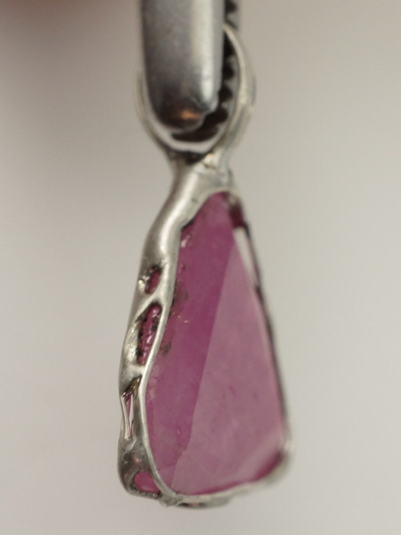 May include: A pink gemstone pendant with a silver setting. The gemstone is faceted and has a triangular shape.