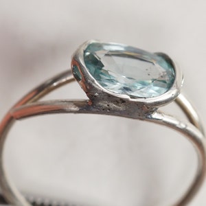 May include: A silver ring with a light blue oval-shaped gemstone set in a bezel setting.