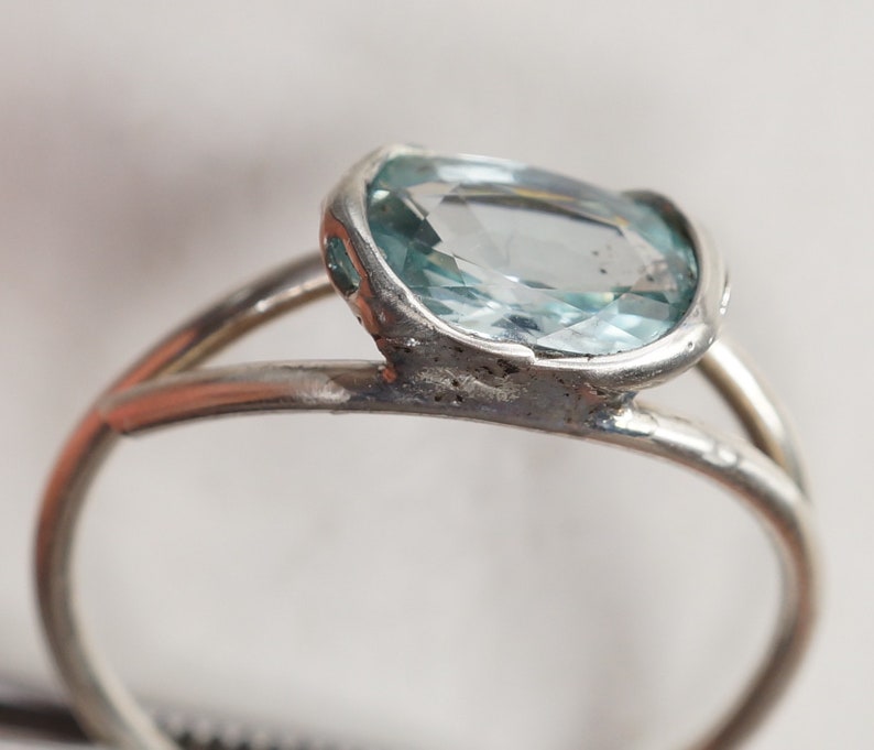 May include: A silver ring with a light blue oval-shaped gemstone set in a bezel setting.