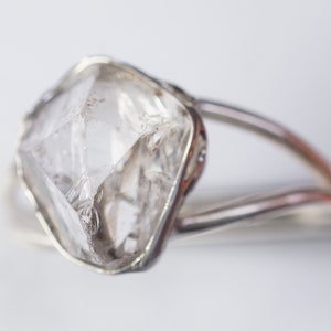 May include: A clear, faceted, diamond-shaped crystal set in a silver ring.