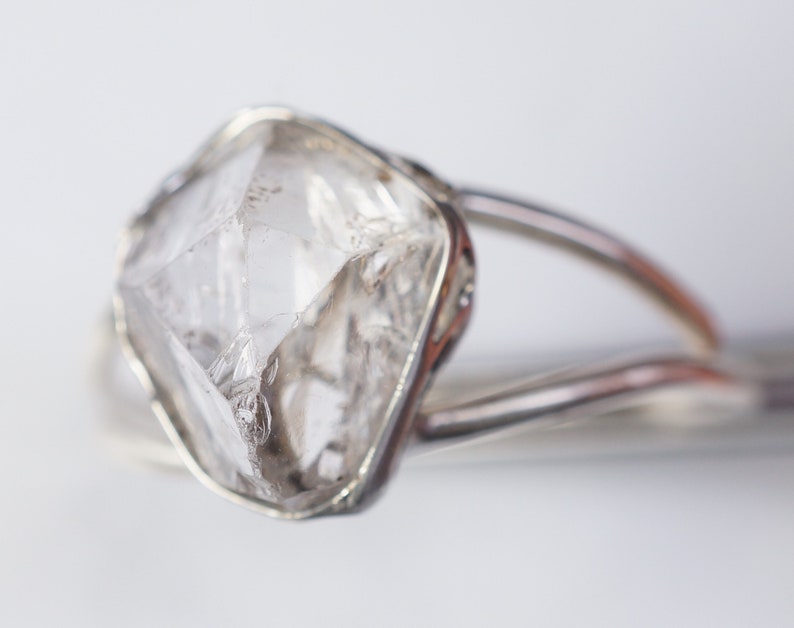 May include: A clear, faceted, diamond-shaped crystal set in a silver ring.