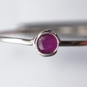 K&ouml;nnte beinhalten: Ein silberner Ring mit einem kleinen, ovalen Rubin, der in einer Zargenfassung gefasst ist.