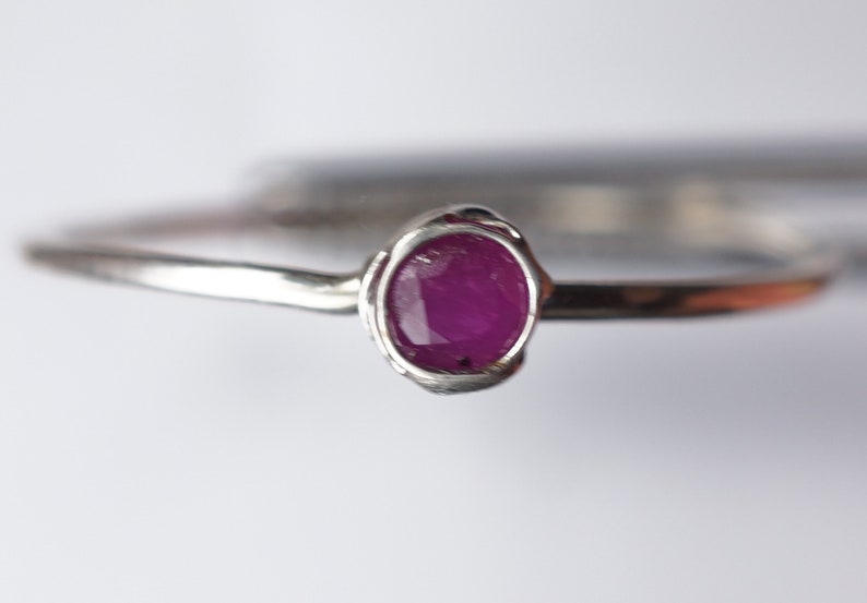 K&ouml;nnte beinhalten: Ein silberner Ring mit einem kleinen, ovalen Rubin, der in einer Zargenfassung gefasst ist.