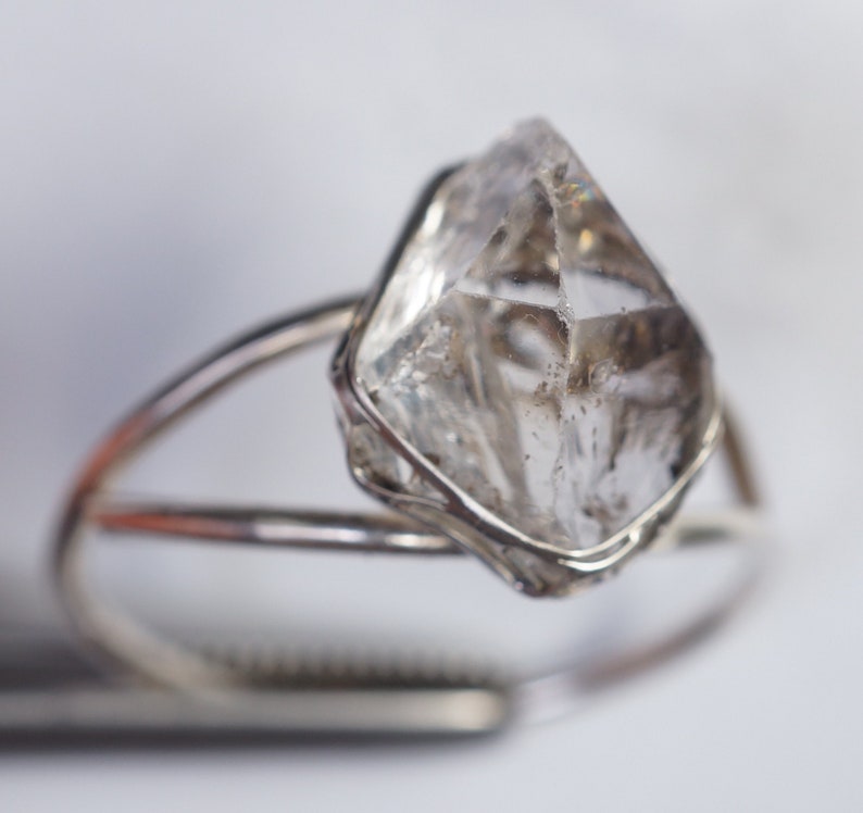 May include: A silver ring with a clear, faceted, crystal-like stone set in a delicate wire cage.
