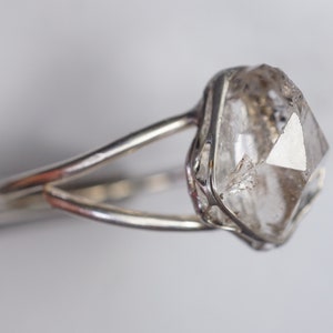 May include: A silver ring with a clear, faceted, octahedral diamond set in a delicate cage.