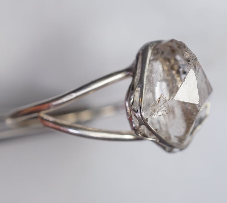May include: A silver ring with a clear, faceted, octahedral diamond set in a delicate cage.