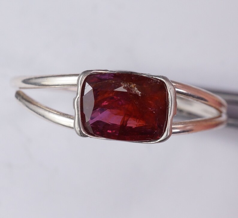 Pu&ograve; includere: Un anello d'argento con una pietra preziosa rettangolare di colore rosso scuro incastonata in una montatura a castone.
