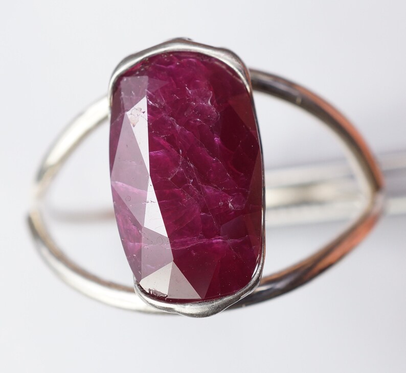Op de afbeelding: Een zilveren ring met een grote, gefacetteerde, rode robijn edelsteen. De robijn is gezet in een bezel setting en heeft een unieke, onregelmatige vorm.