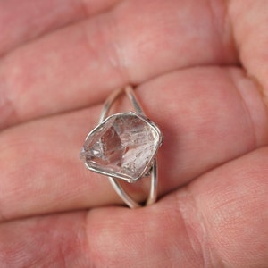 May include: A silver ring with a clear quartz crystal set in the center. The crystal is faceted and has a rough, natural look.
