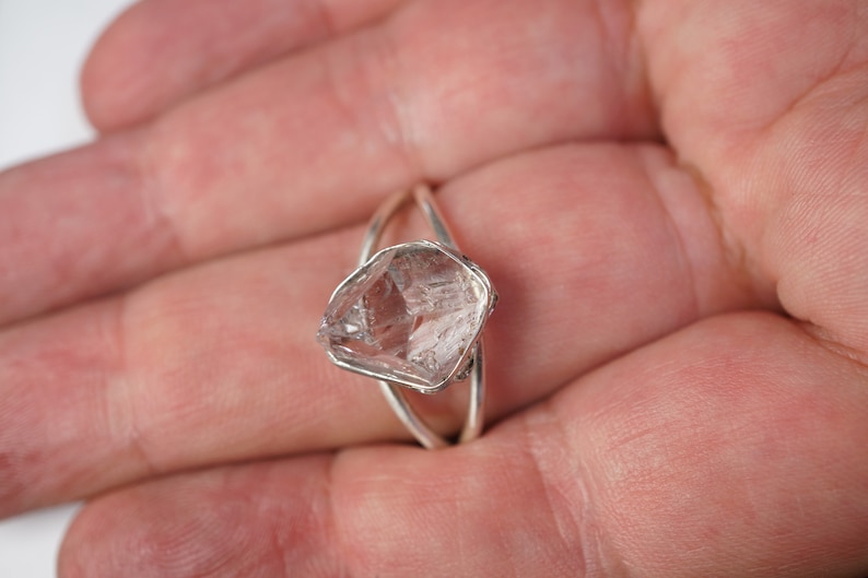 May include: A silver ring with a clear quartz crystal set in the center. The crystal is faceted and has a rough, natural look.