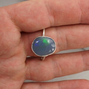 May include: A silver ring with a blue opal gemstone. The opal has green and black flashes of color.