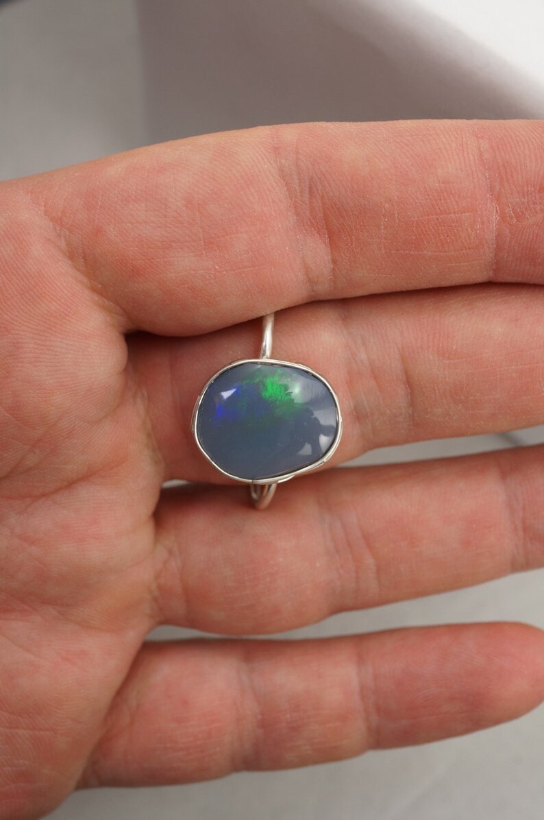 May include: A silver ring with a blue opal gemstone. The opal has green and black flashes of color.