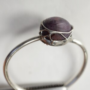 May include: A silver ring with a purple gemstone set in a delicate wire cage design.