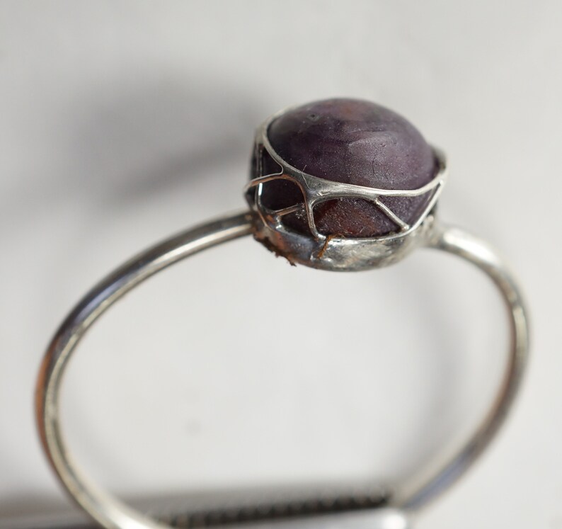 May include: A silver ring with a purple gemstone set in a delicate wire cage design.