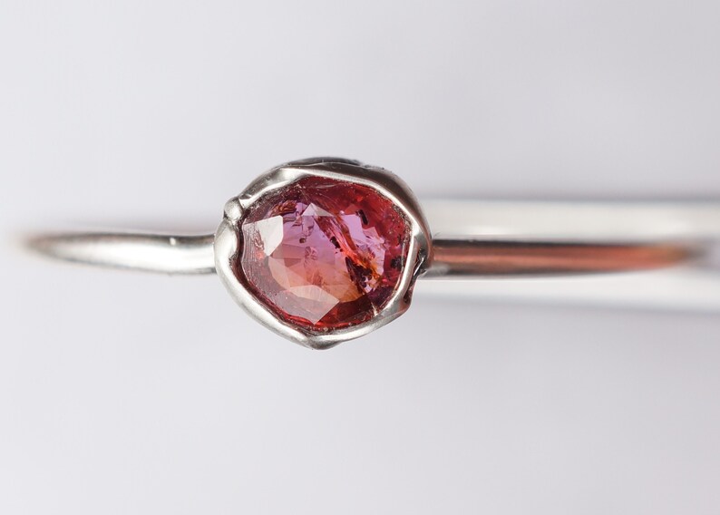 Op de afbeelding: Een zilveren ring met een roze edelsteen in een bezel setting.