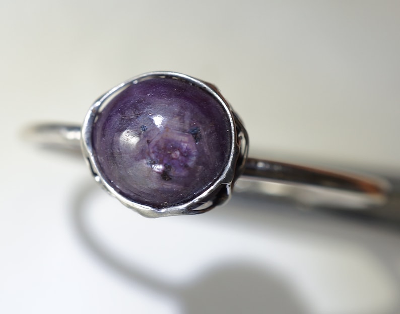 May include: A silver ring with a purple gemstone set in a bezel setting.