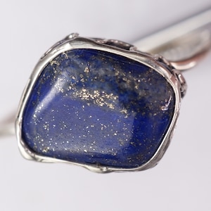 Puede incluir: Un anillo de plata con una gran piedra de lapisl&aacute;zuli azul engastada en un engaste de bisel. La piedra tiene una textura brillante y brillante.