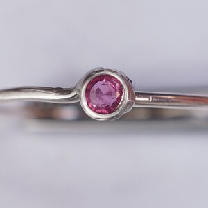 K&ouml;nnte beinhalten: Ein schlichter Silberring mit einem kleinen, runden, rosafarbenen Edelstein in der Mitte.