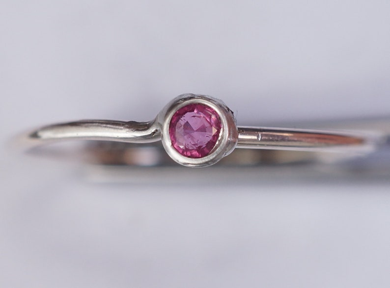 K&ouml;nnte beinhalten: Ein schlichter Silberring mit einem kleinen, runden, rosafarbenen Edelstein in der Mitte.