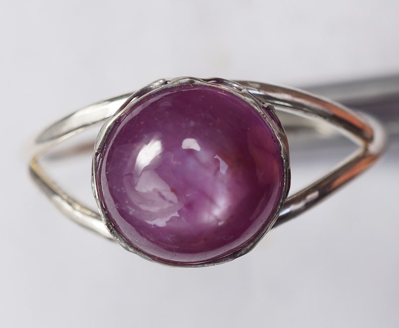 May include: A silver ring with a large, round, cabochon-cut, pink ruby gemstone.