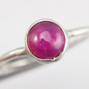 May include: A silver ring with a pink gemstone set in a bezel setting.