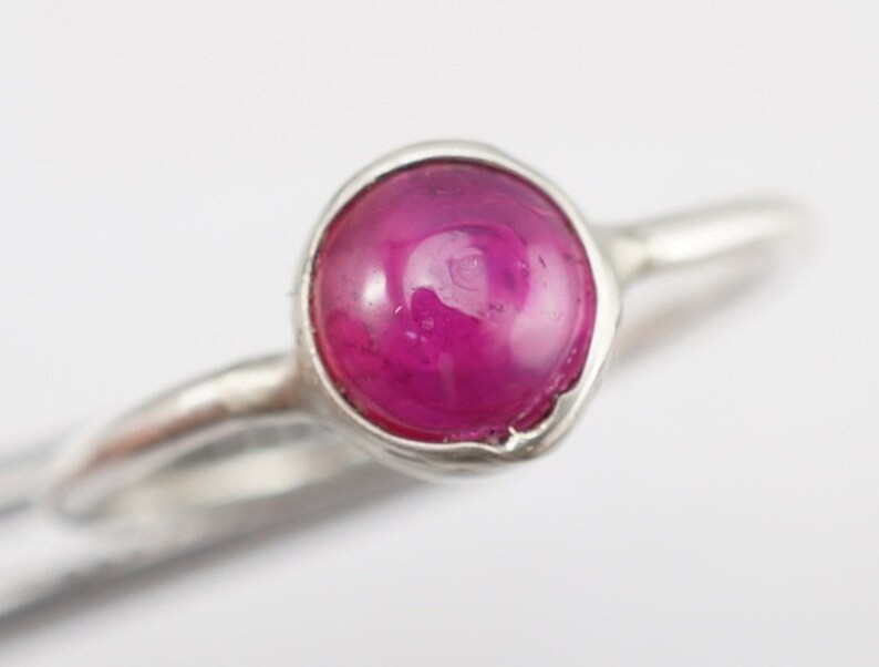 May include: A silver ring with a pink gemstone set in a bezel setting.