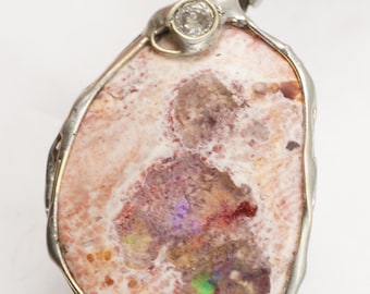May include: A silver pendant featuring a pink opal with iridescent flashes of color, set in a silver frame with a small diamond accent.