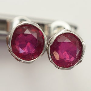 May include: A pair of silver earrings with small, round, faceted ruby red gemstones.