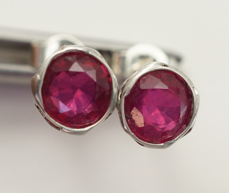 May include: A pair of silver earrings with small, round, faceted ruby red gemstones.