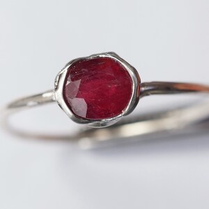 Pode incluir: Um anel de prata com uma gema vermelha engastada em uma moldura texturizada.