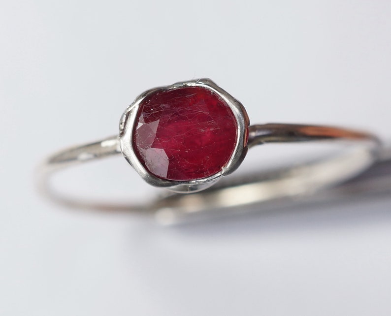 Pode incluir: Um anel de prata com uma gema vermelha engastada em uma moldura texturizada.