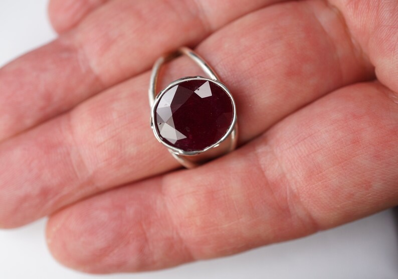 May include: A silver ring with a large, faceted ruby gemstone set in a bezel setting. The ring has a delicate, twisted band.