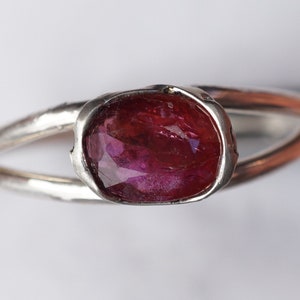 Puede incluir: Un anillo de plata con una piedra ovalada de color rosa oscuro engastada en un engaste texturizado.
