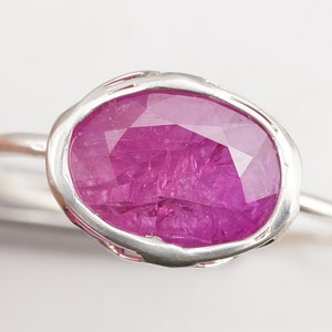 Op de afbeelding: Een zilveren ring met een grote, gefacetteerde, roze robijn gezet in een getextureerde, ovale zetting.