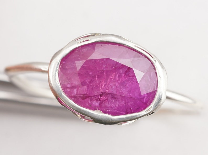 Op de afbeelding: Een zilveren ring met een grote, gefacetteerde, roze robijn gezet in een getextureerde, ovale zetting.
