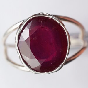 May include: A silver ring with a large, faceted, dark red ruby gemstone.