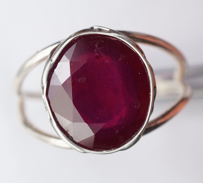 May include: A silver ring with a large, faceted, dark red ruby gemstone.