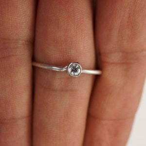 May include: A silver ring with a small, clear gemstone set in a bezel setting.
