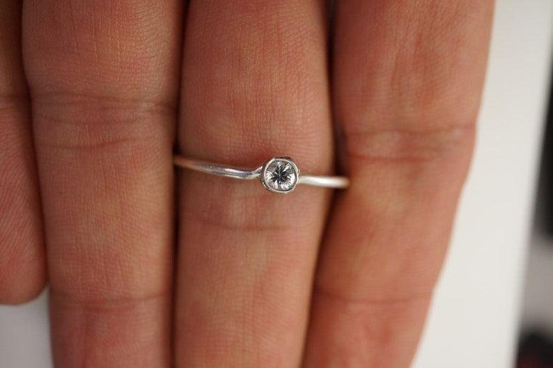 May include: A silver ring with a small, clear gemstone set in a bezel setting.