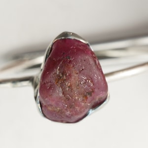 May include: A silver ring with a large, rough, dark red ruby gemstone.