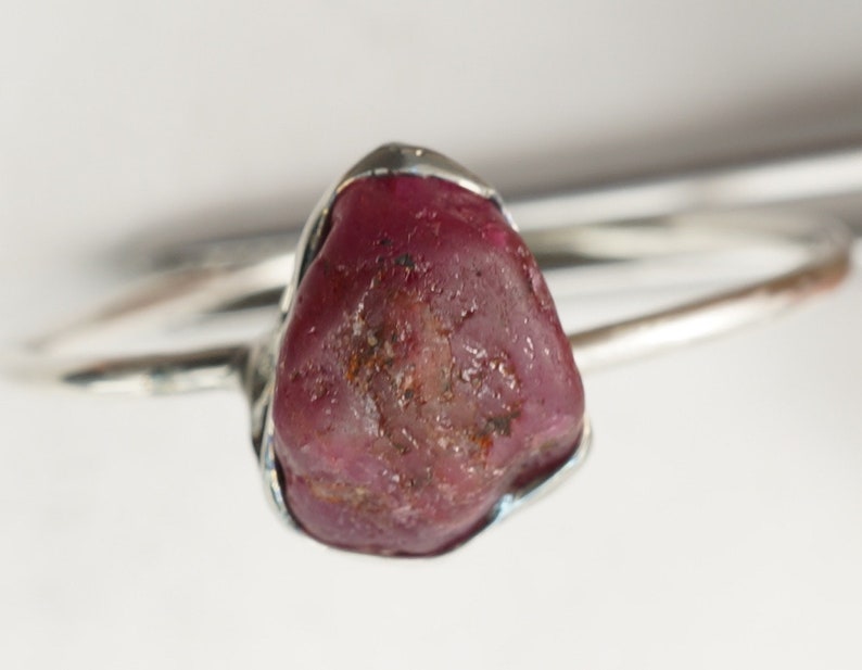 May include: A silver ring with a large, rough, dark red ruby gemstone.