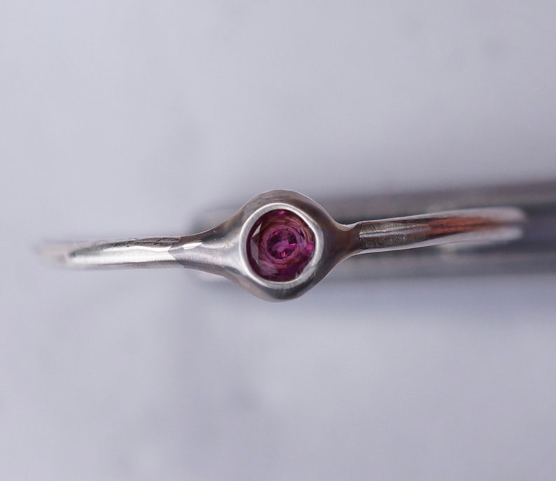 Puede incluir: Un anillo de plata con una sola piedra preciosa redonda y p&uacute;rpura engastada en un engaste de bisel.