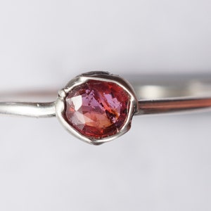 Op de afbeelding: Een zilveren ring met een roze en rode edelsteen in een bezel-setting.